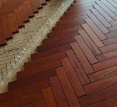 Herringbone wooden flooring being installed over underlayment and backing material.